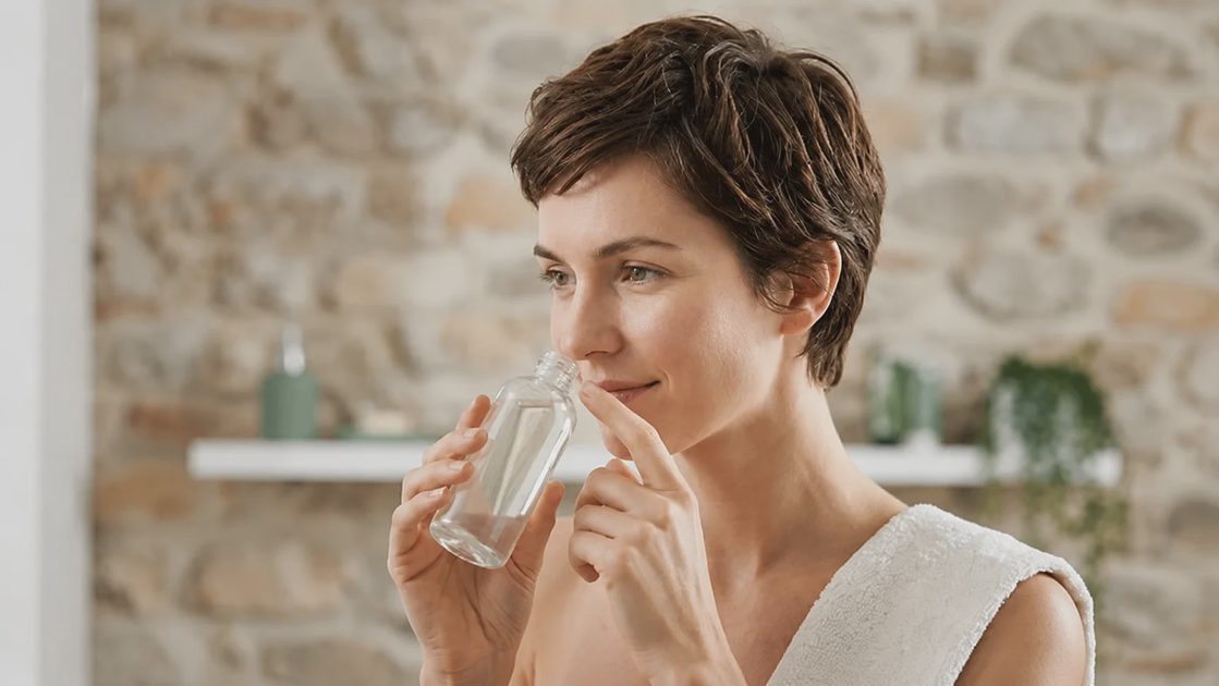 smelling a bottle of clear clarifying shampoo in a neutral bathroom setup.webp